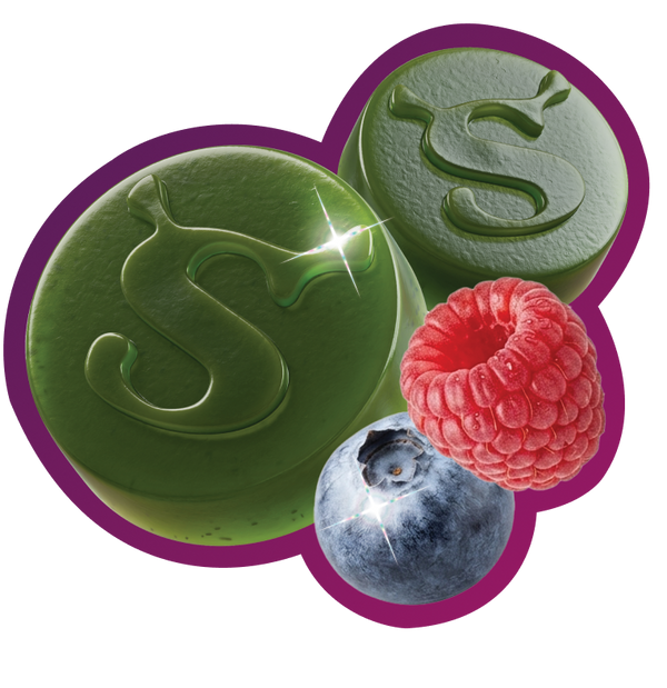 Two green gummies embossed with an 'S' logo, next to a fresh raspberry and blueberry, transparent background.