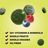 Two green gummies embossed with an S logo, next to a raspberry and blueberry, above a checklist reading 20+ Vitamins & Minerals, Whole Fruits, Whole Veggies, and 4g Fiber, on a yellow-green background.