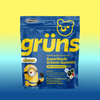 Blue Grüns Superfoods Greens Gummies bag in Bello Banana Berry flavor with Minions branding, on a yellow-to-blue gradient background