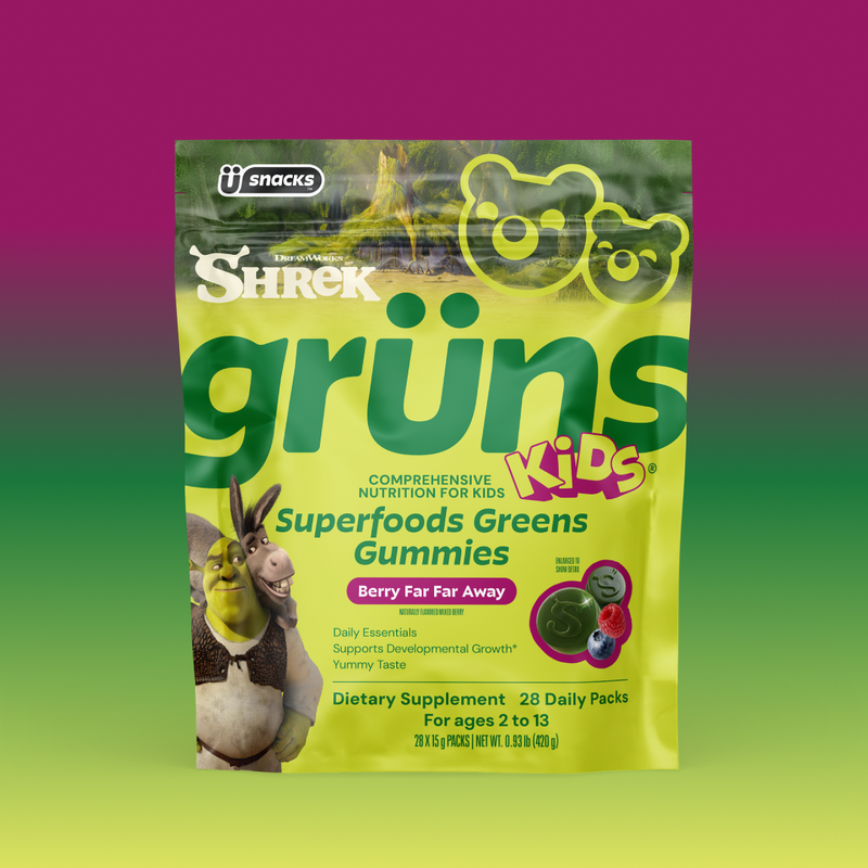 Yellow-green Shrek Kids Grüns Superfoods Greens Gummies package featuring Shrek and Donkey, labeled Berry Far Far Away flavor, listing Daily Essentials, Supports Developmental Growth, Yummy Taste, Dietary Supplement, 28 Daily Packs, for ages 2 to 13, on a purple-to-green gradient background.
