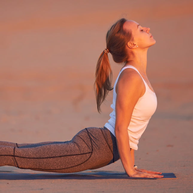 Woman practicing yoga on a sandy beach at sunset