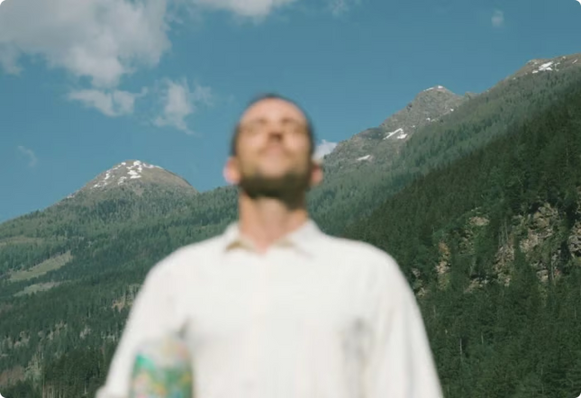 Man standing in front of a mountainous landscape with green trees and blue sky.
