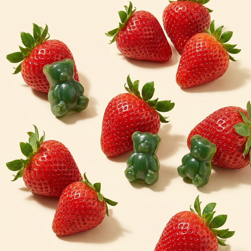 Green gummy bears scattered among fresh strawberries on a cream background