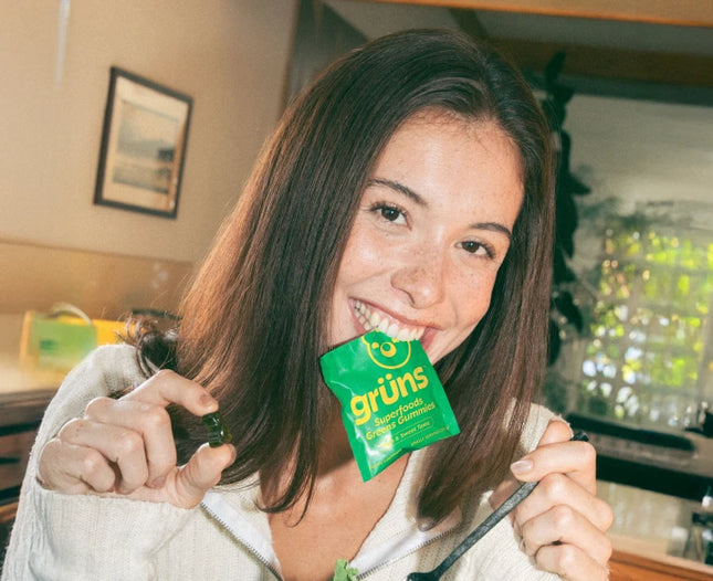 Woman biting Grüns sachet and holding a Grüns gummy