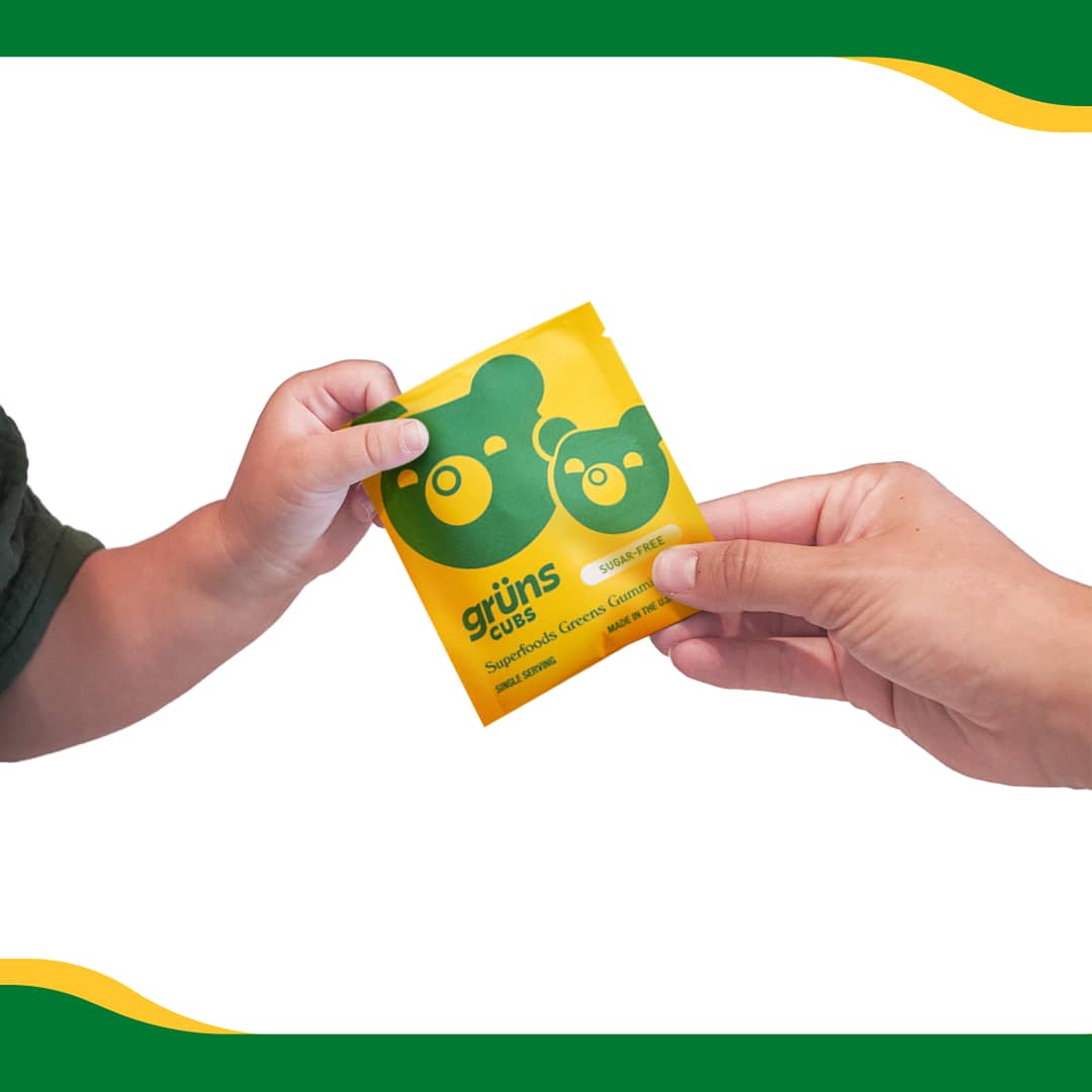 Two hands exchanging a yellow packet labeled 'grüns cubs' with bear illustrations.