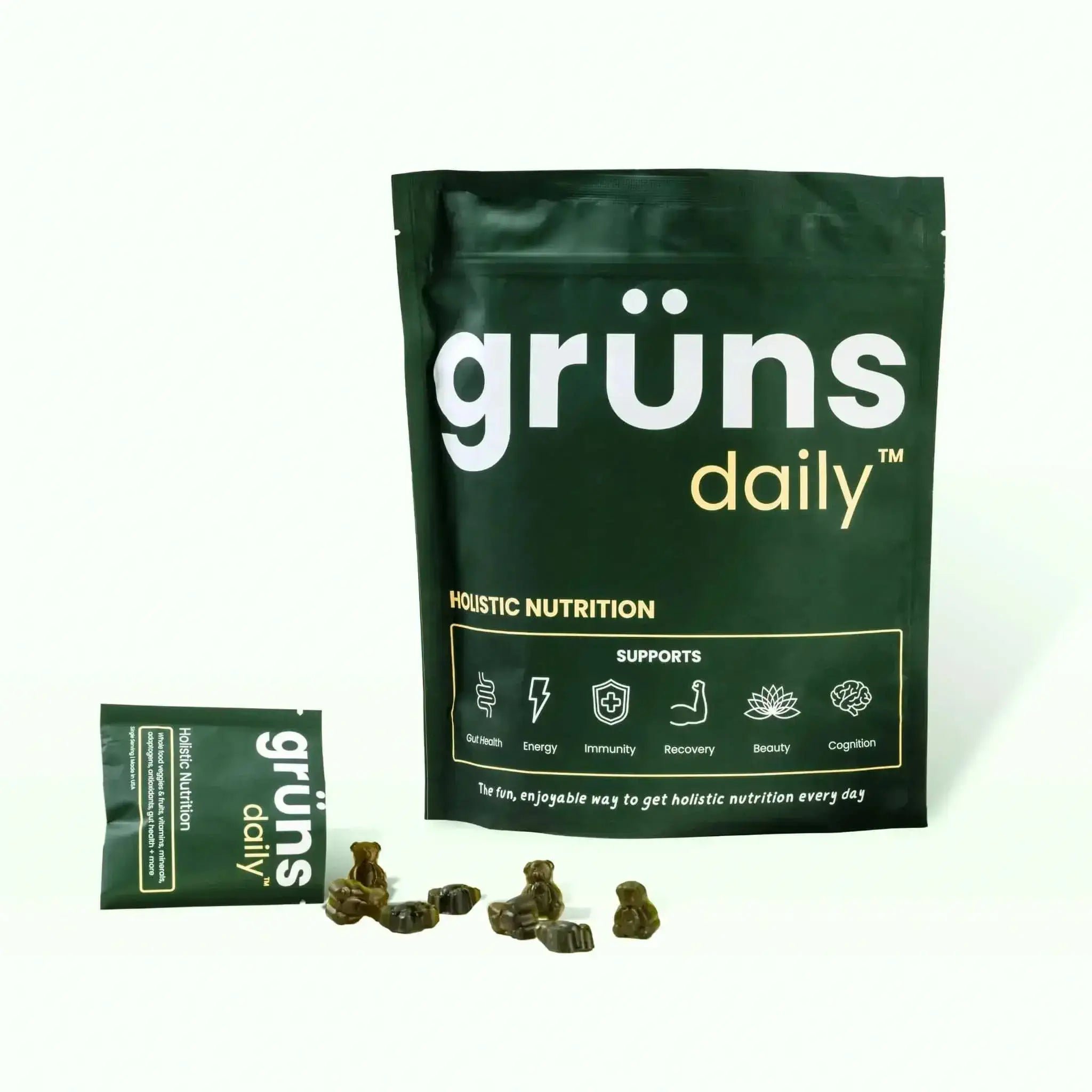 Packaging of 'grüns daily' holistic nutrition supplement with spilled supplements in the foreground.