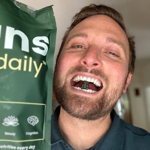 Man holding a green-packaged product while showing contents in his mouth with a smile.
