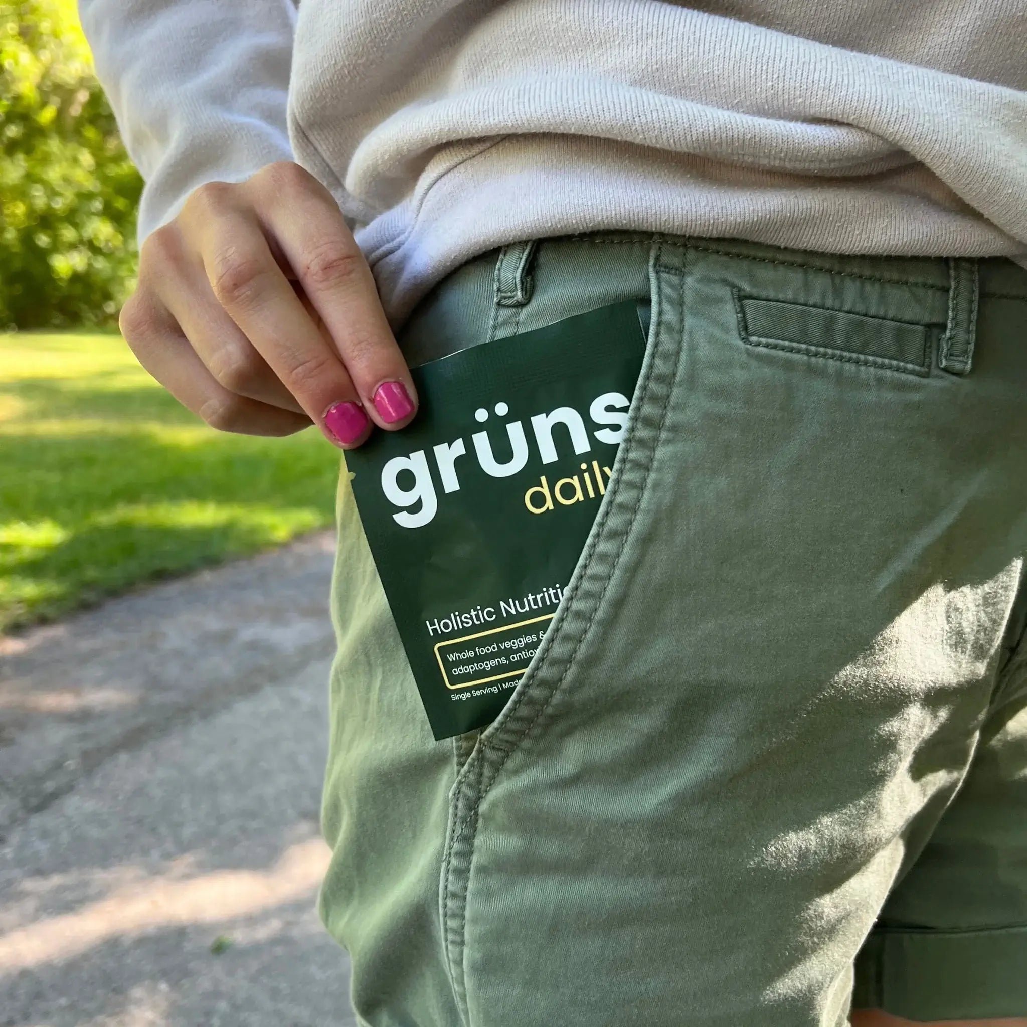Hand placing a 'grüns daily' packet into green shorts pocket.