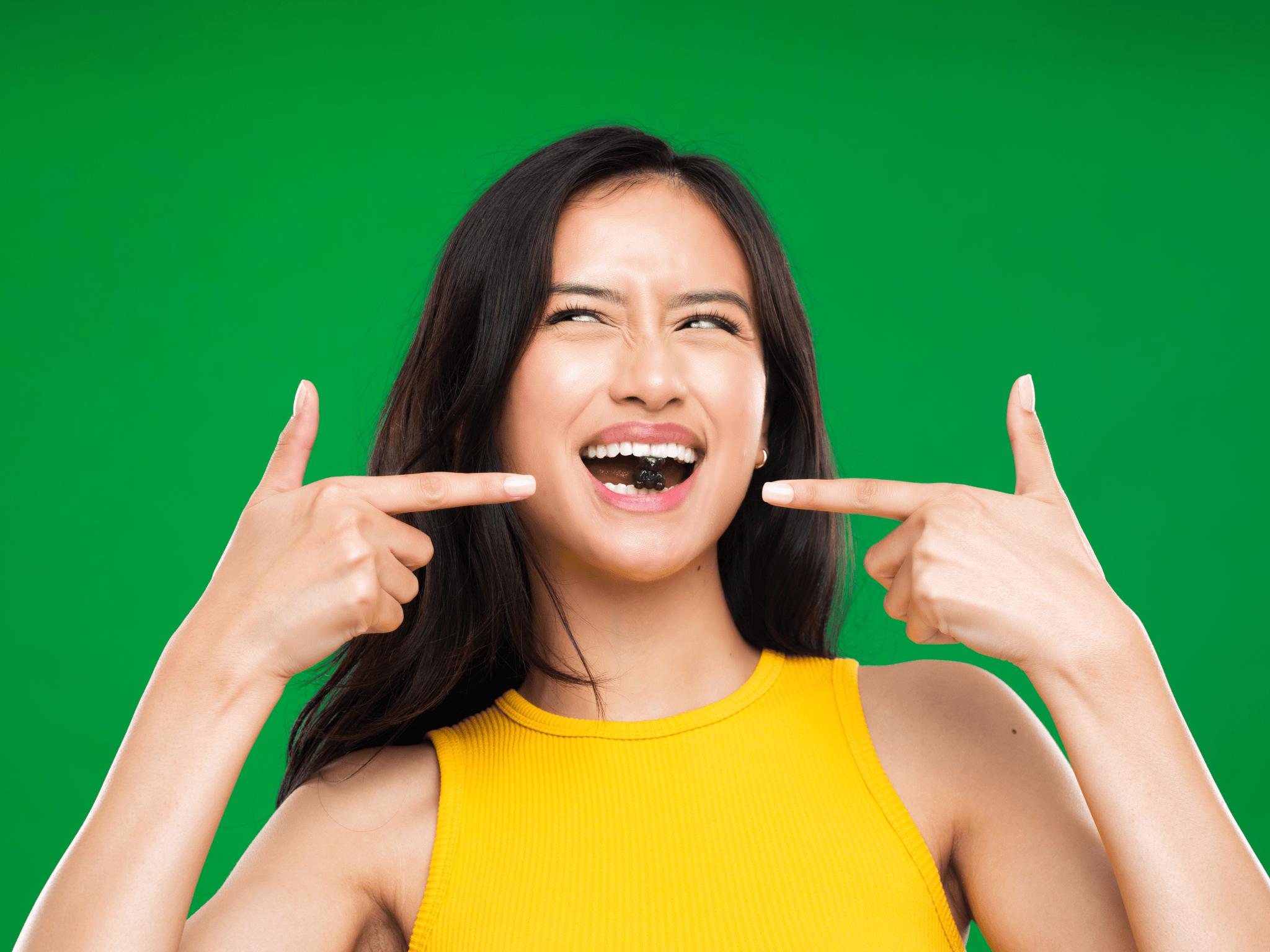 Woman smiling and pointing at her braces against a green background.
