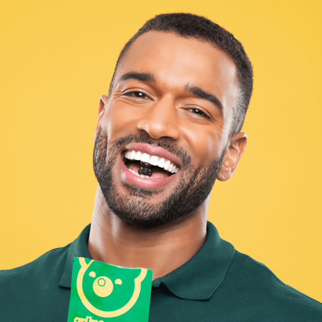 Man smiling while holding a piece of candy in mouth against a yellow background.