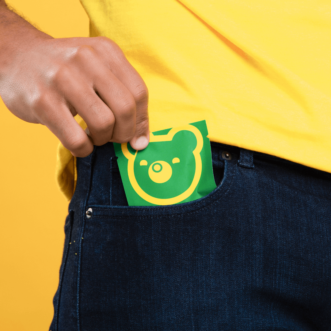 Hand slipping green packet with bear logo into a denim pocket.