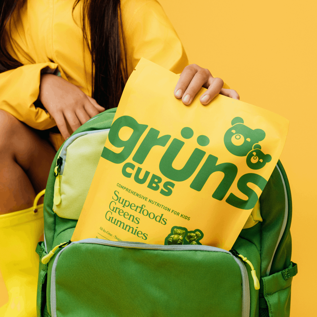 A person in a yellow jacket holding a green backpack with grüns CUBS gummies.