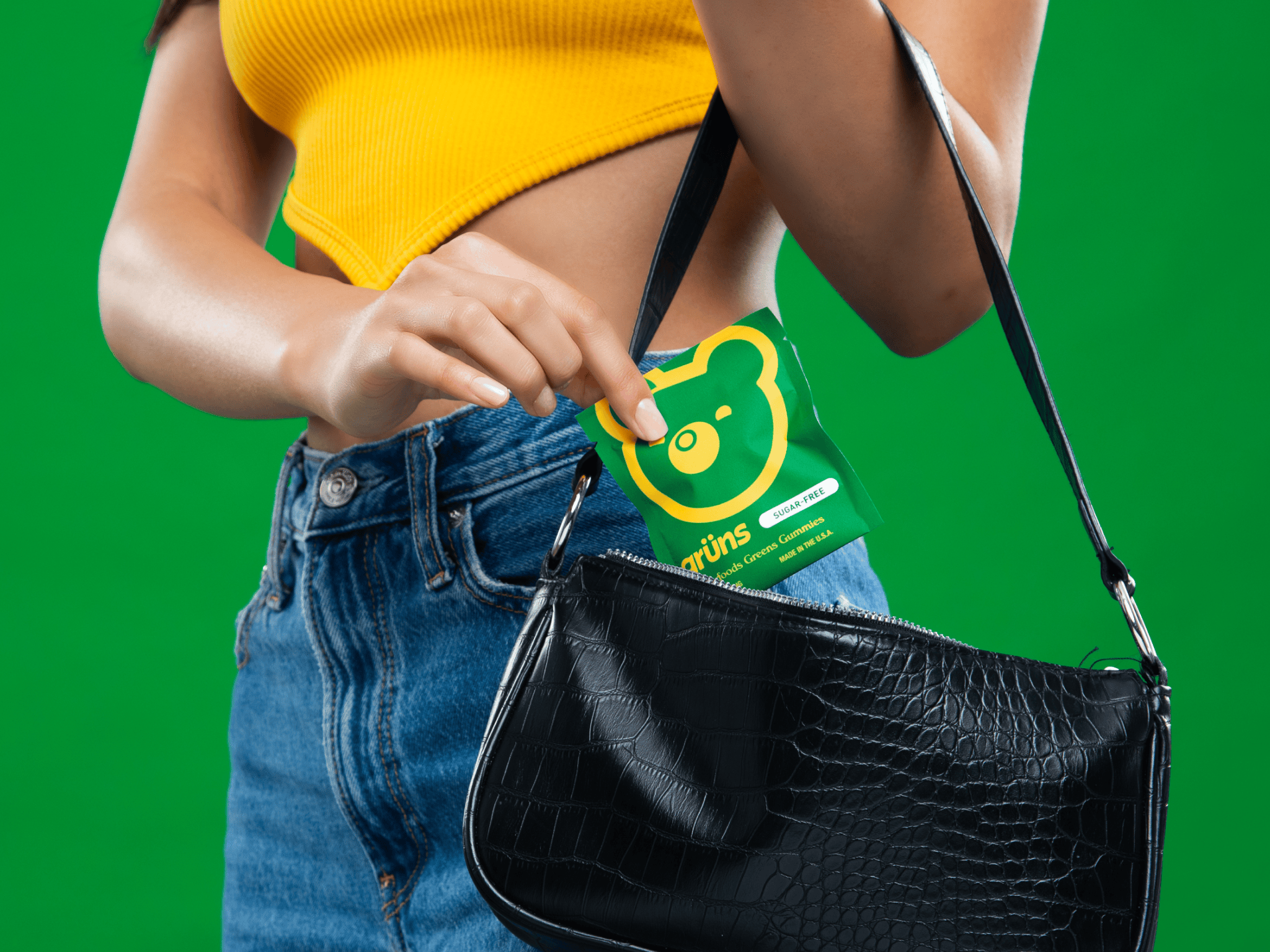 Person putting a green packet into a black handbag against a green background.