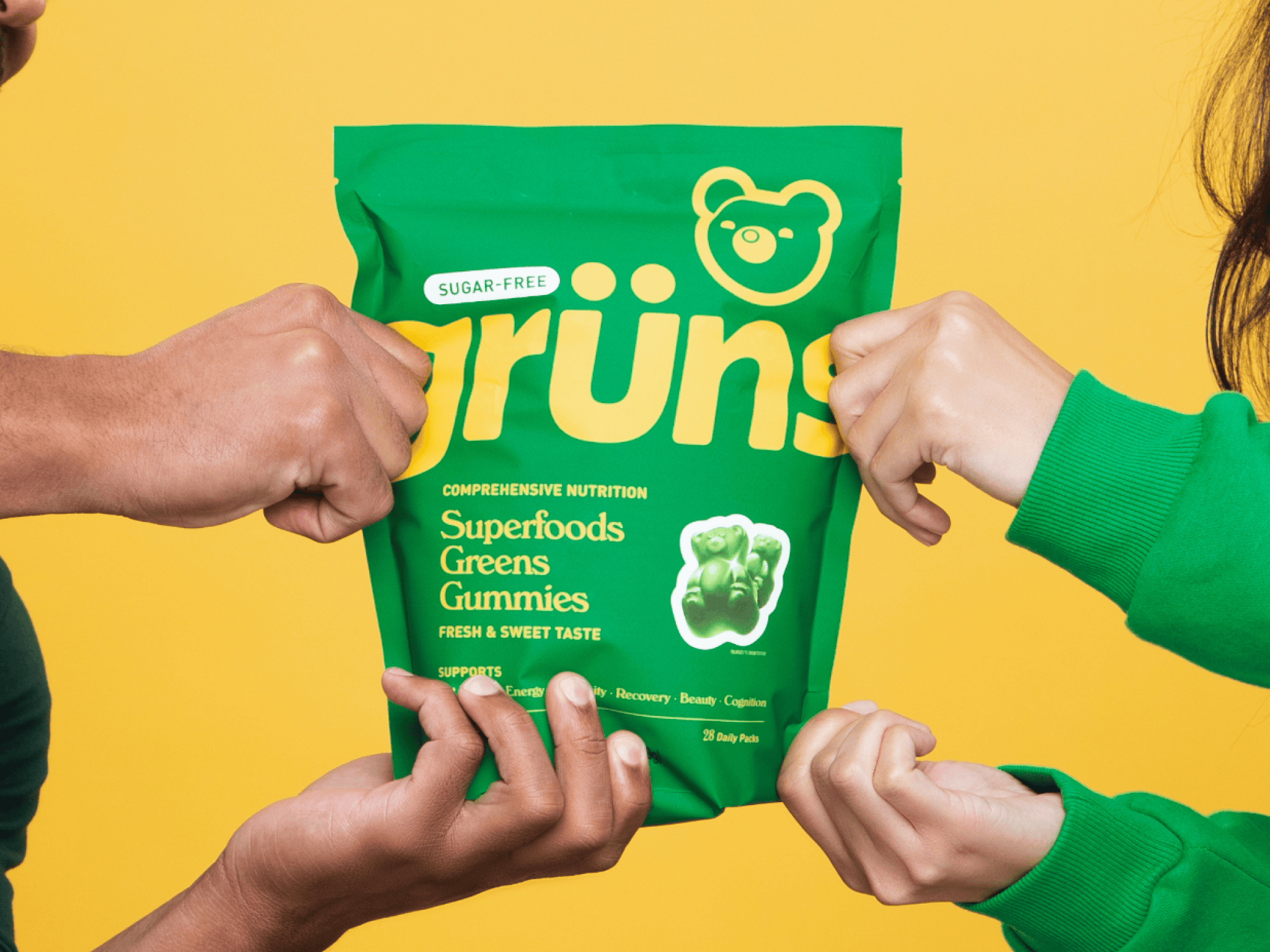 Hands holding a green package of sugar-free superfoods greens gummies.