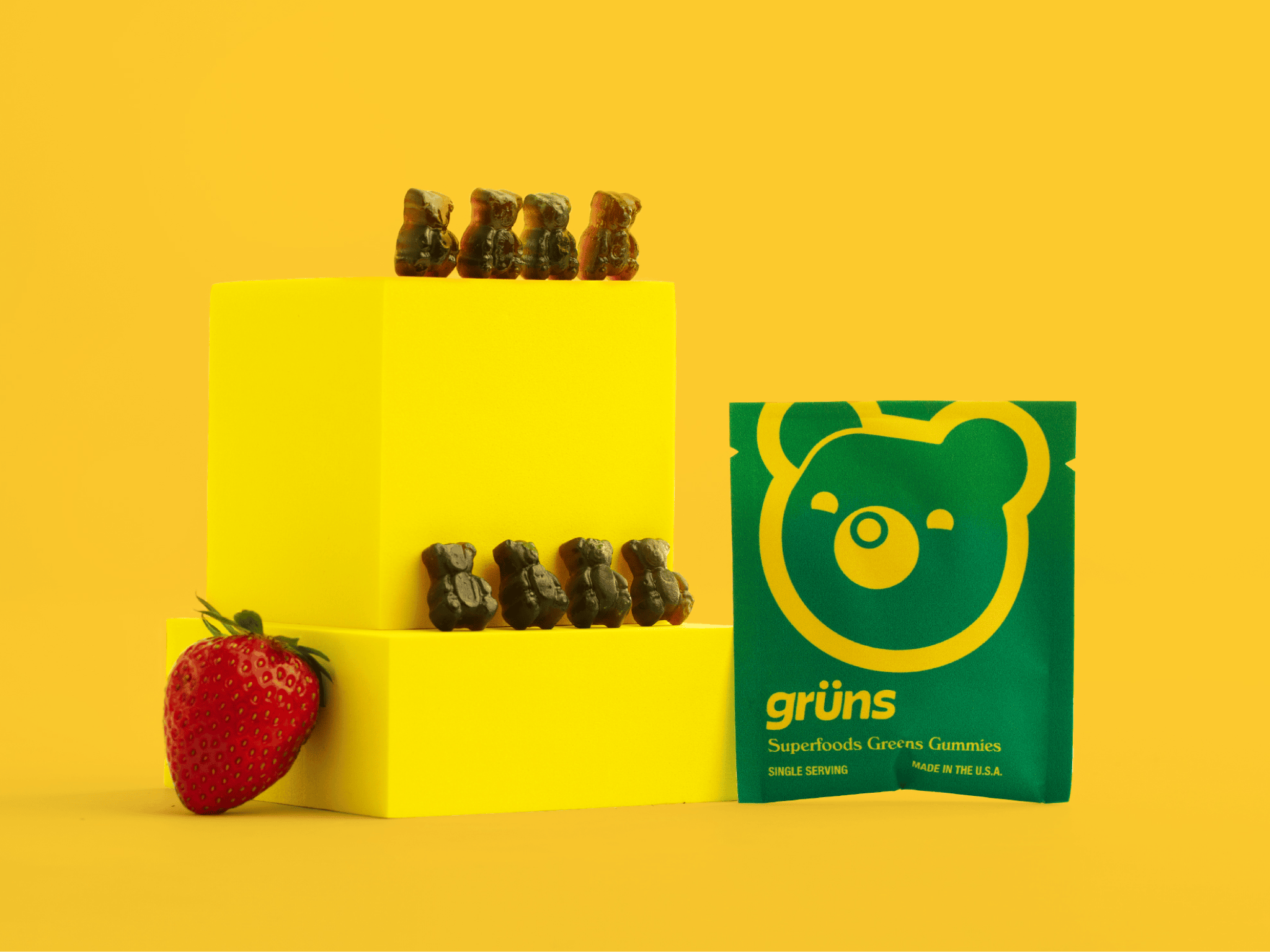 Gummy bears on yellow blocks with a strawberry and a green bear-packaged snack.
