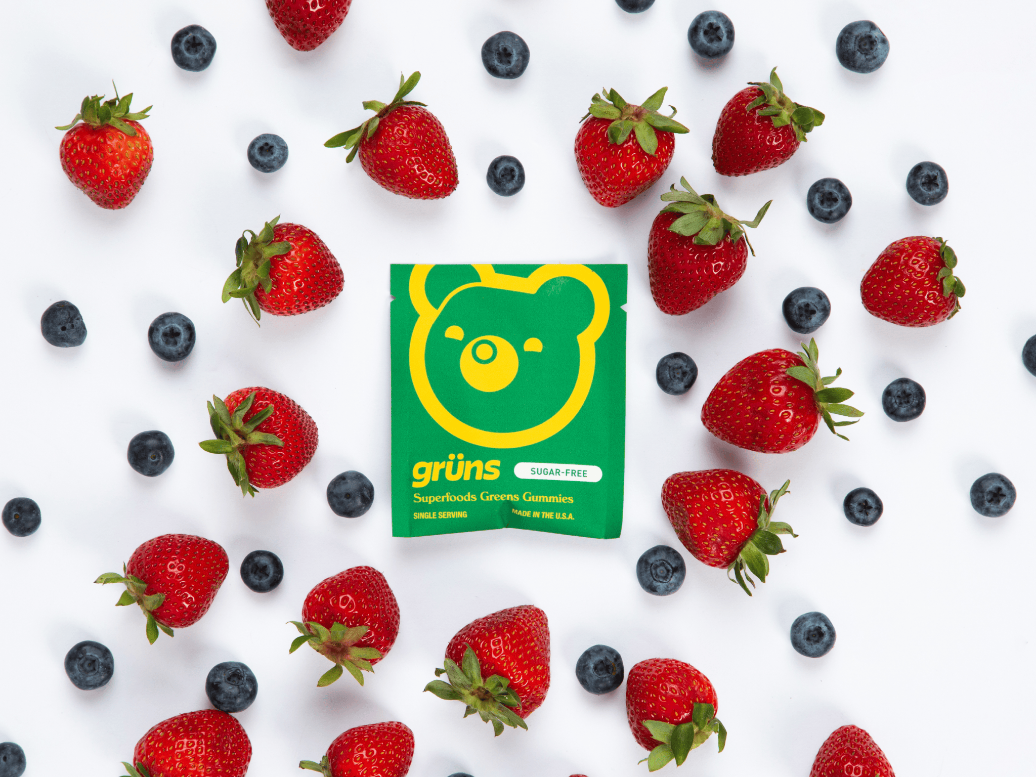 Green gummy package surrounded by strawberries and blueberries.