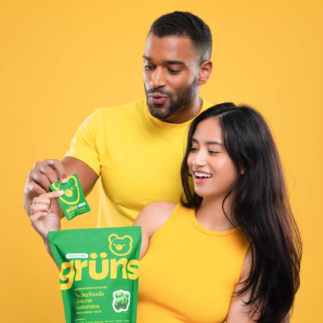 Two people enjoying Grüns superfood gummies, wearing matching yellow outfits against a yellow background.