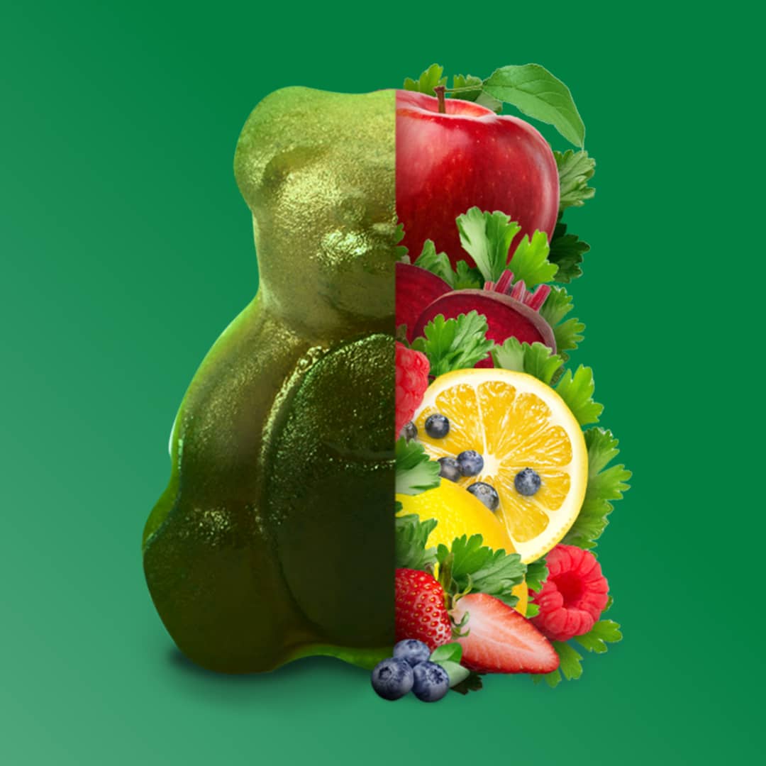 Half gummy bear, half assorted fruits and vegetables on a green background.